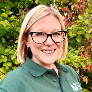Headshot of a woman in a Chilterns National Landscape shirt in front of green foliage.