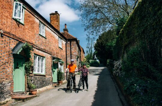 Two cyclists in a quaint village street of red bricked houses