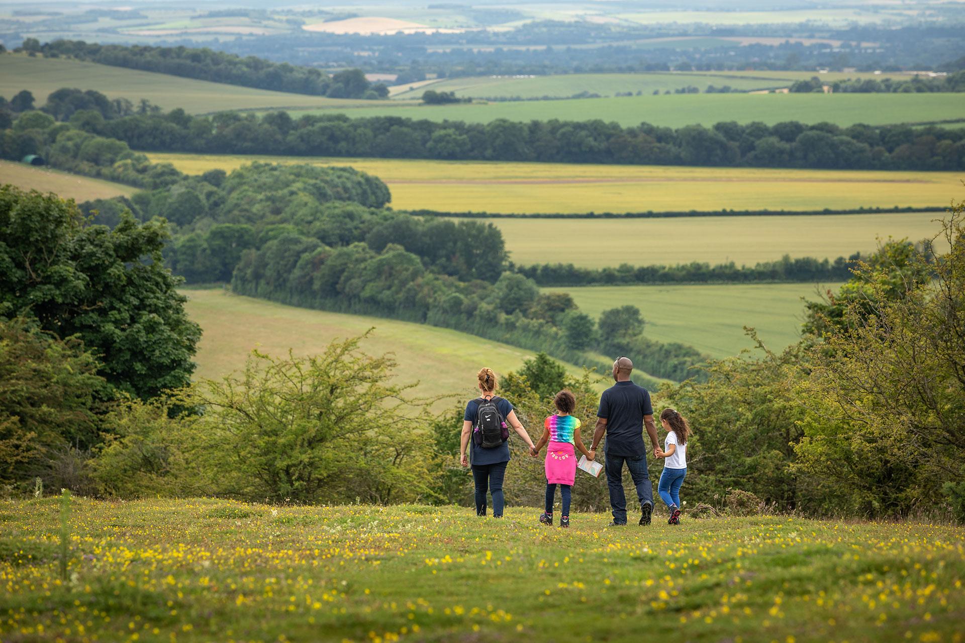 A family of four people going for a walk together in the chilterns countryside. They are surroinded by hills, fields and woodlands.
