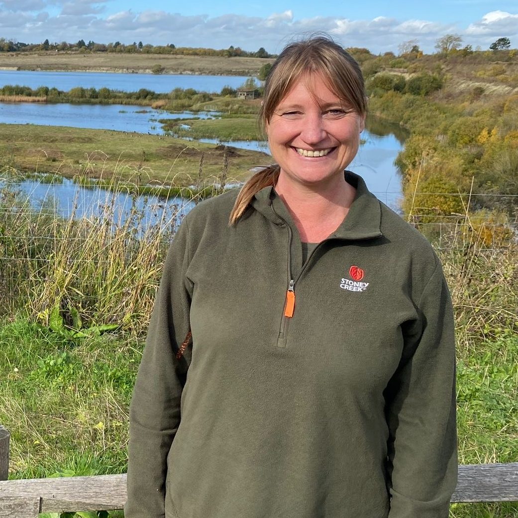 A woman wearing a green fleece standing in front of a lake.