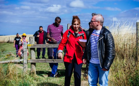 A man and woman walk through a field ahead of a group of people.