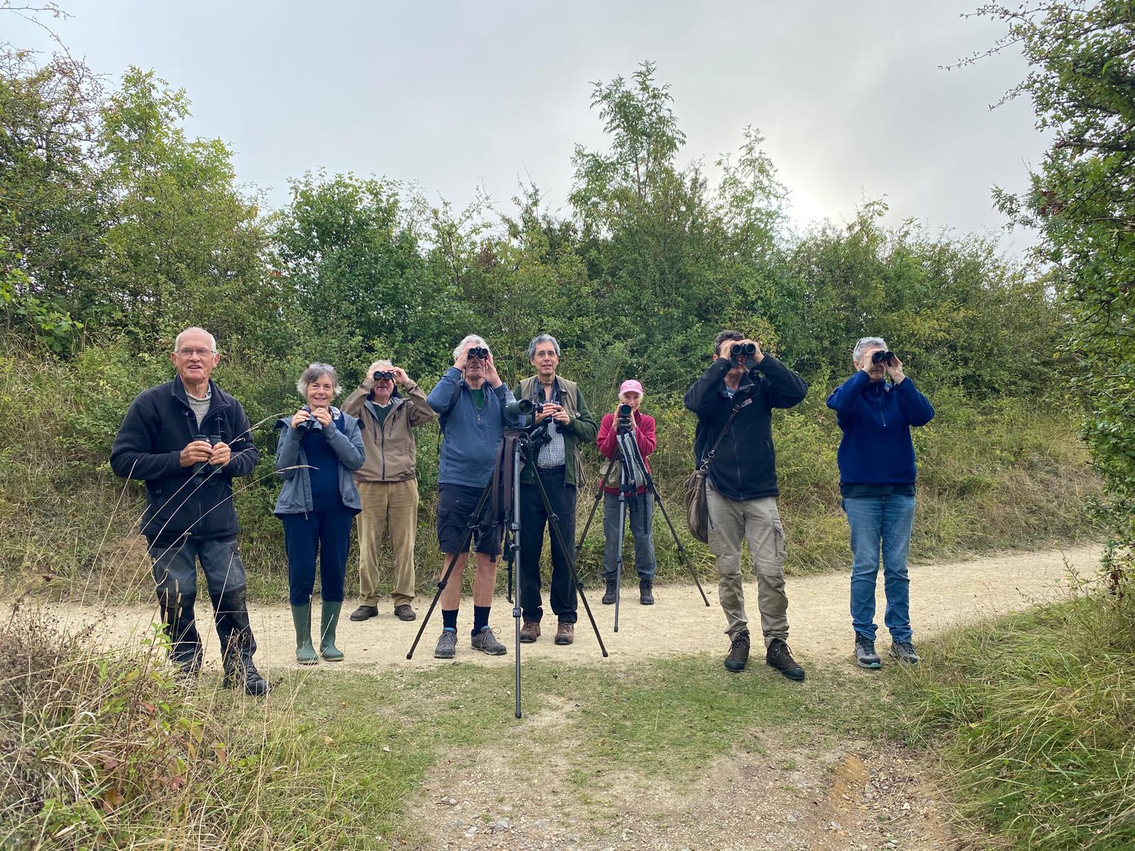 group of people looking through binoculars straight at the camera in a rural setting