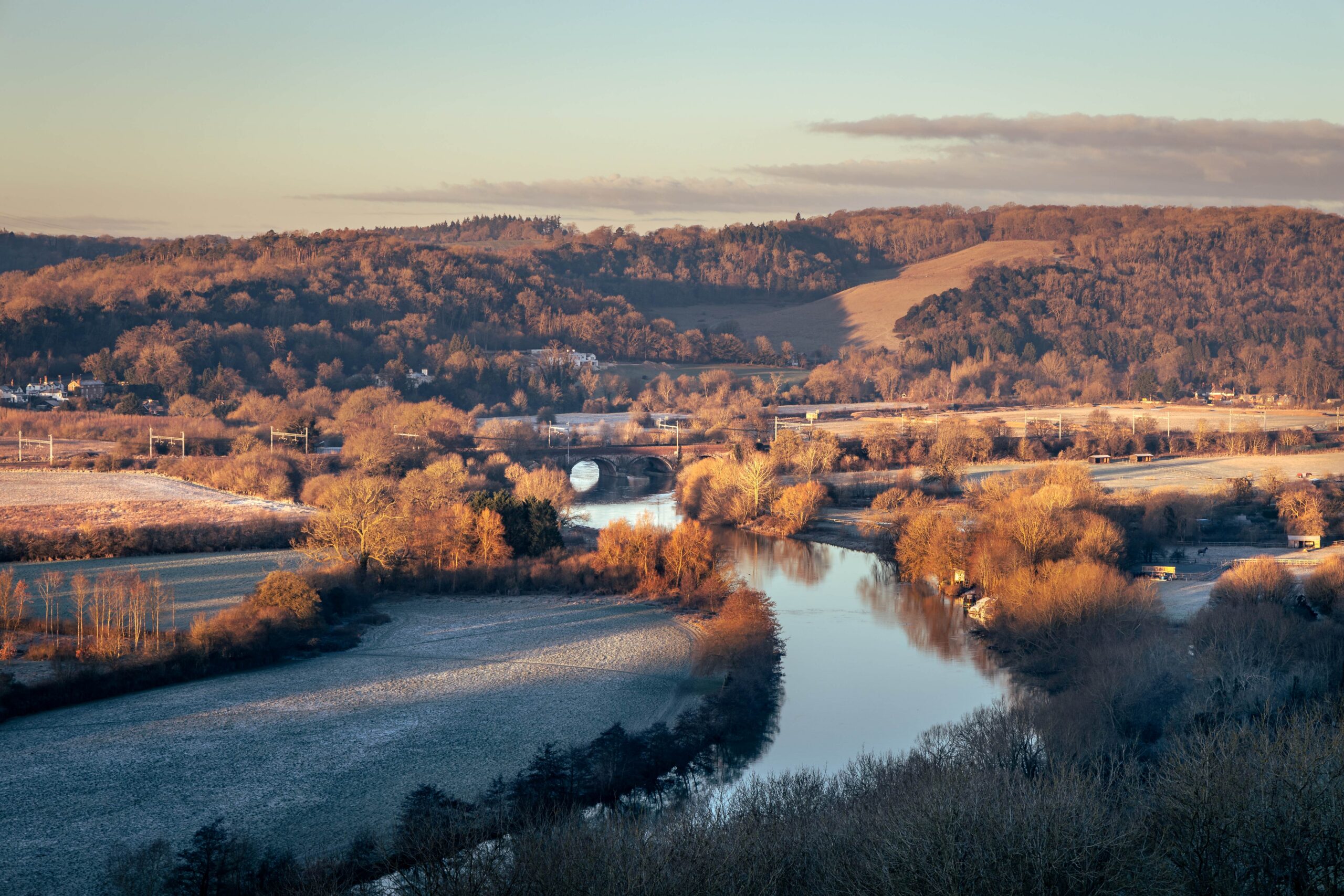 Frosty sunrise image of a river winding through fields with woodlands in the distance.