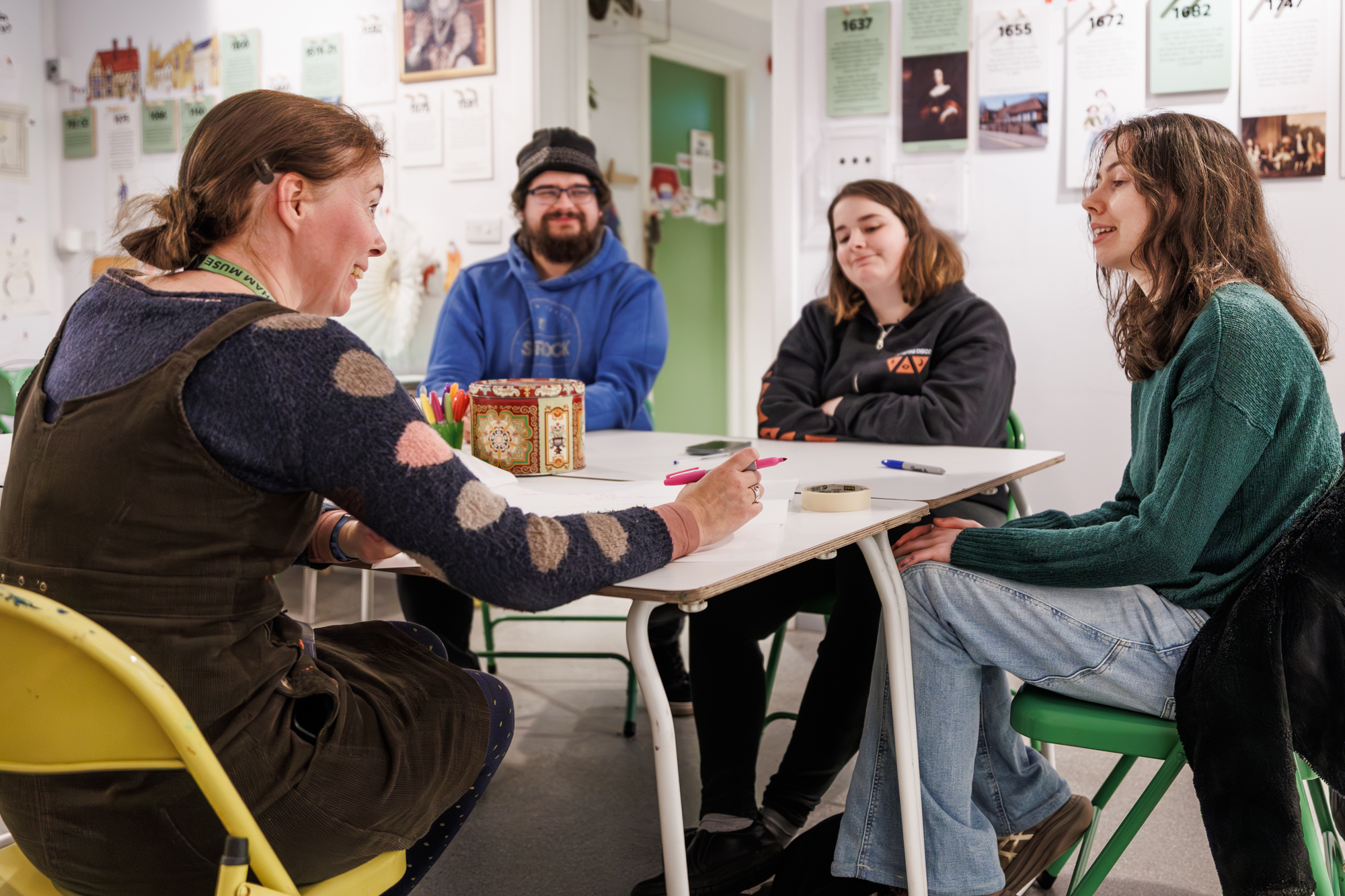 Two young women and a young man sit at a table and talk to a woman who is writing things on a large piece of paper.