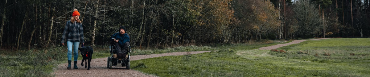 A woman walks a dog alongside a person in a mobility scooter.
