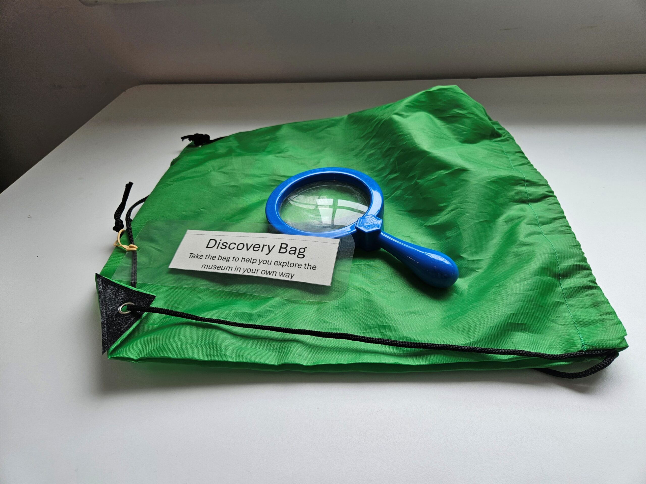 A green drawstring bag with a blue magnifying glass and a label with the words "Discovery Bag".