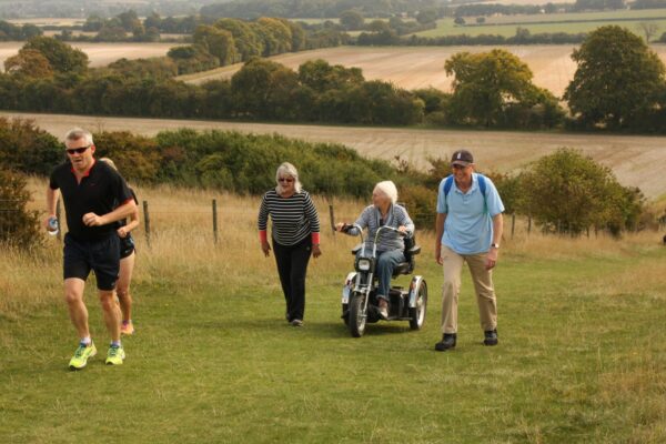 A man jogs in front of 3 elderly people on a hill. One is in a mobility scooter.