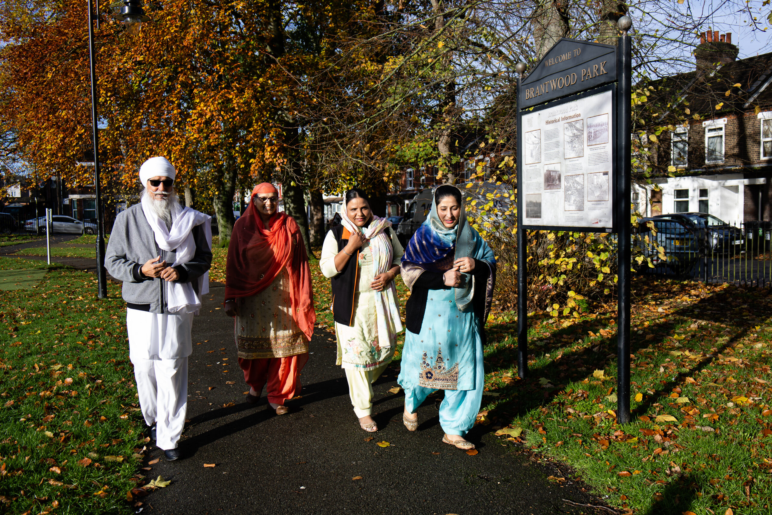 A group of 4 people walking through a park. The man is wearing a white turban and the women are wearing colourful Sikh clothing.