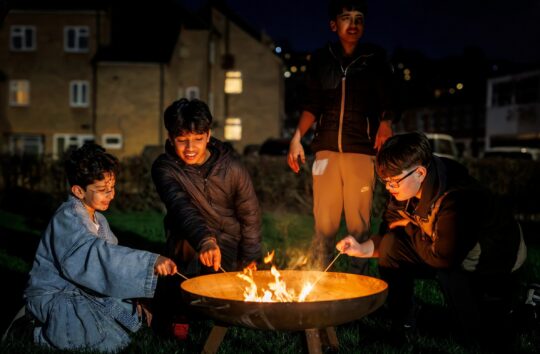 Four young boys toasting marshmallows around a campfire