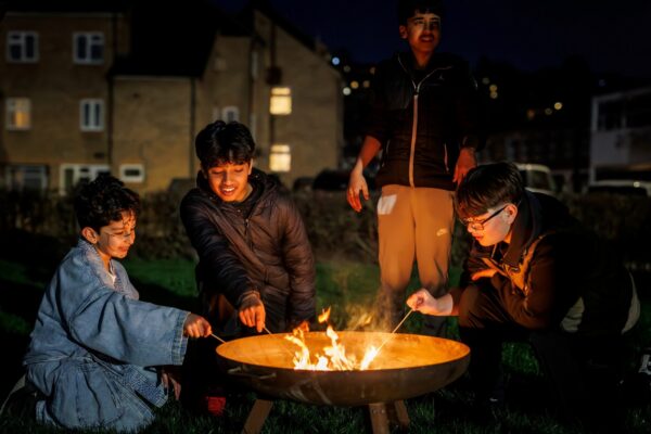 Four young boys toasting marshmallows around a campfire