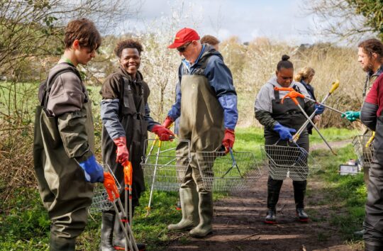 group of young adults doing a river clean wearing waders and using litter pickers