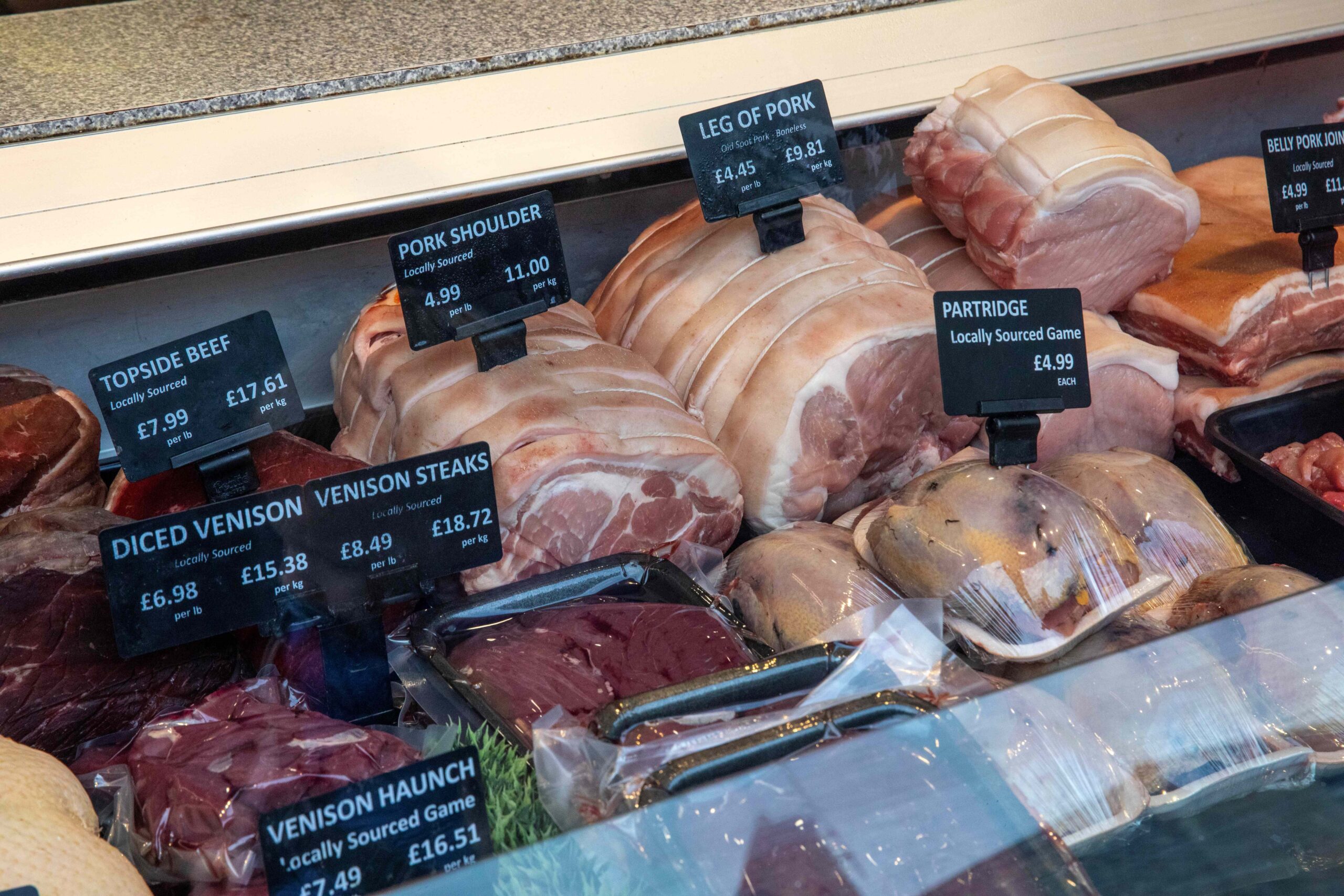 A butcher's counter with different cuts of meat, one labelled as venison.