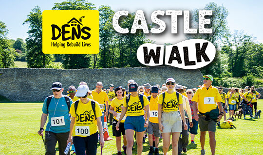 A group of people wearing yellow tshirts walk past a castle, the words "DENS Castle Walk" are written in white over the top of the image.