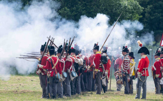 A group of people dressed in red Household Cavalry uniforms with smoke in the background.