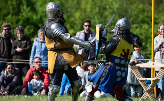 Two people dressed up as Medieval knights in chainmail as a crowd watches on.