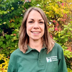 Headshot of a woman in a Chilterns National Landscape shirt in front of green foliage