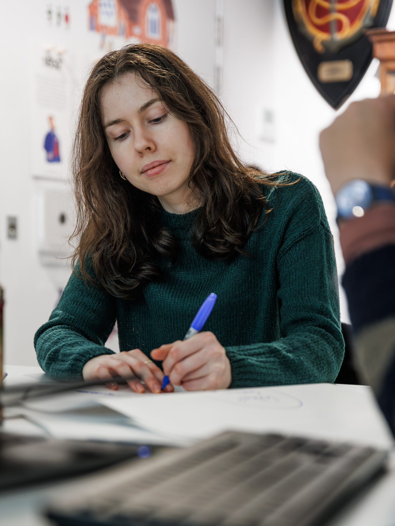 A young woman writes on a large piece of paper in a blue marker pen.