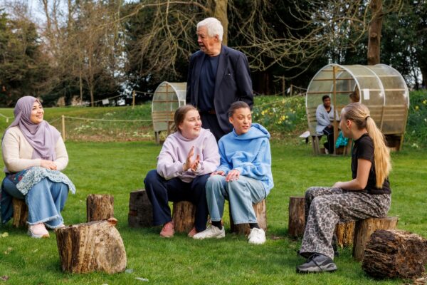 A group of four teenage girls sit on stumps in a garden chatting and laughing