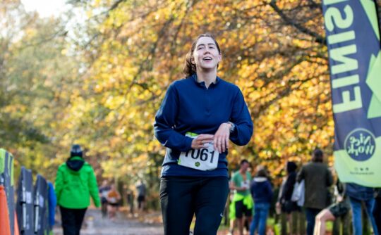 A female runner crosses the finish line in a woodland.