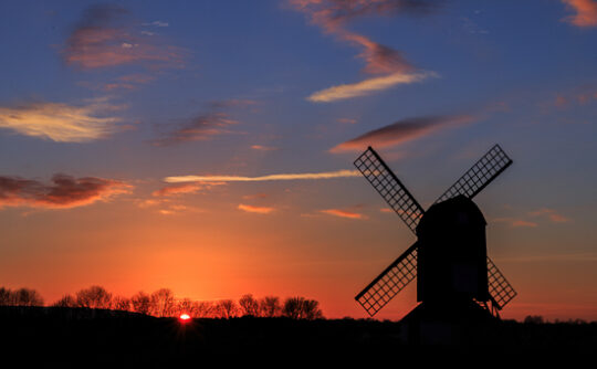 Silhouette of a windmill in a field at sunset.