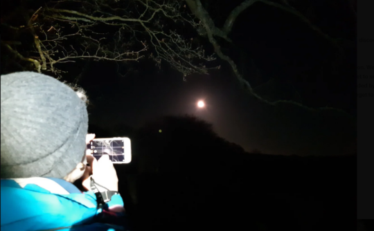 Person taking a photo of the moon at night