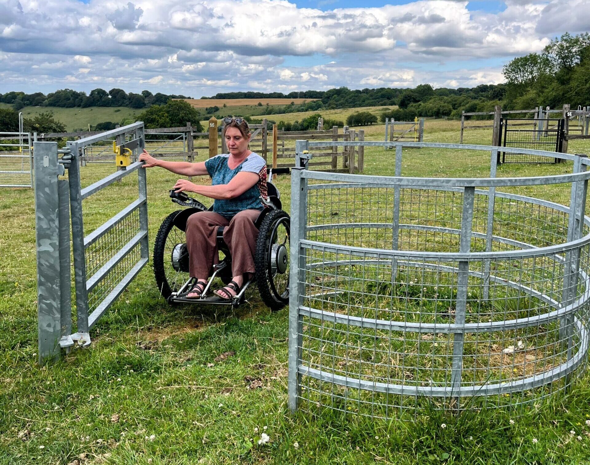 Woman in a wheelchair using an accessible gate in a field.