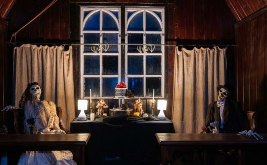Dark room with window and two skeletons lit by candlelight