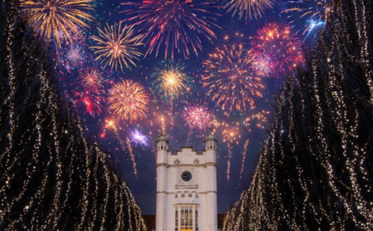 White hotel flanked by tree lined avenue with fireworks lighting up the sky